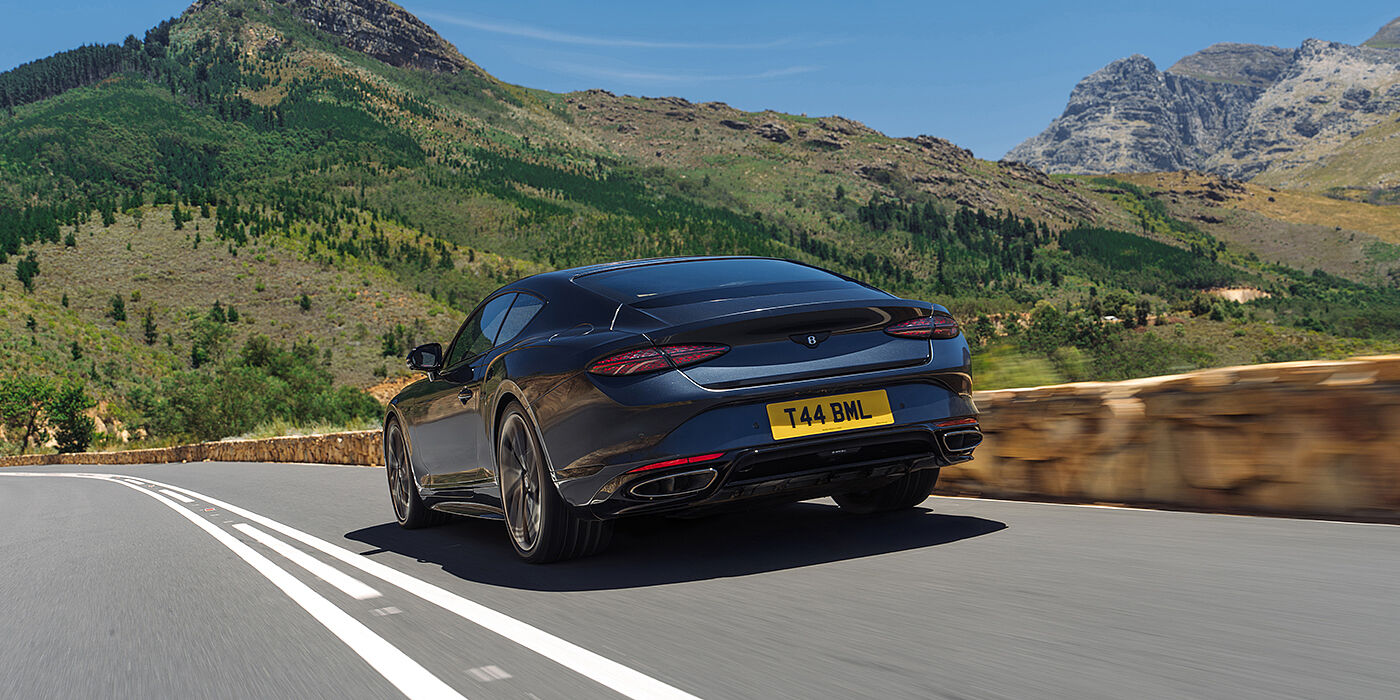 Gohm Sportwagen GmbH | Bentley Singen Bentley Continental GT coupe in Thunder paint rear driving through mountains in sunshine