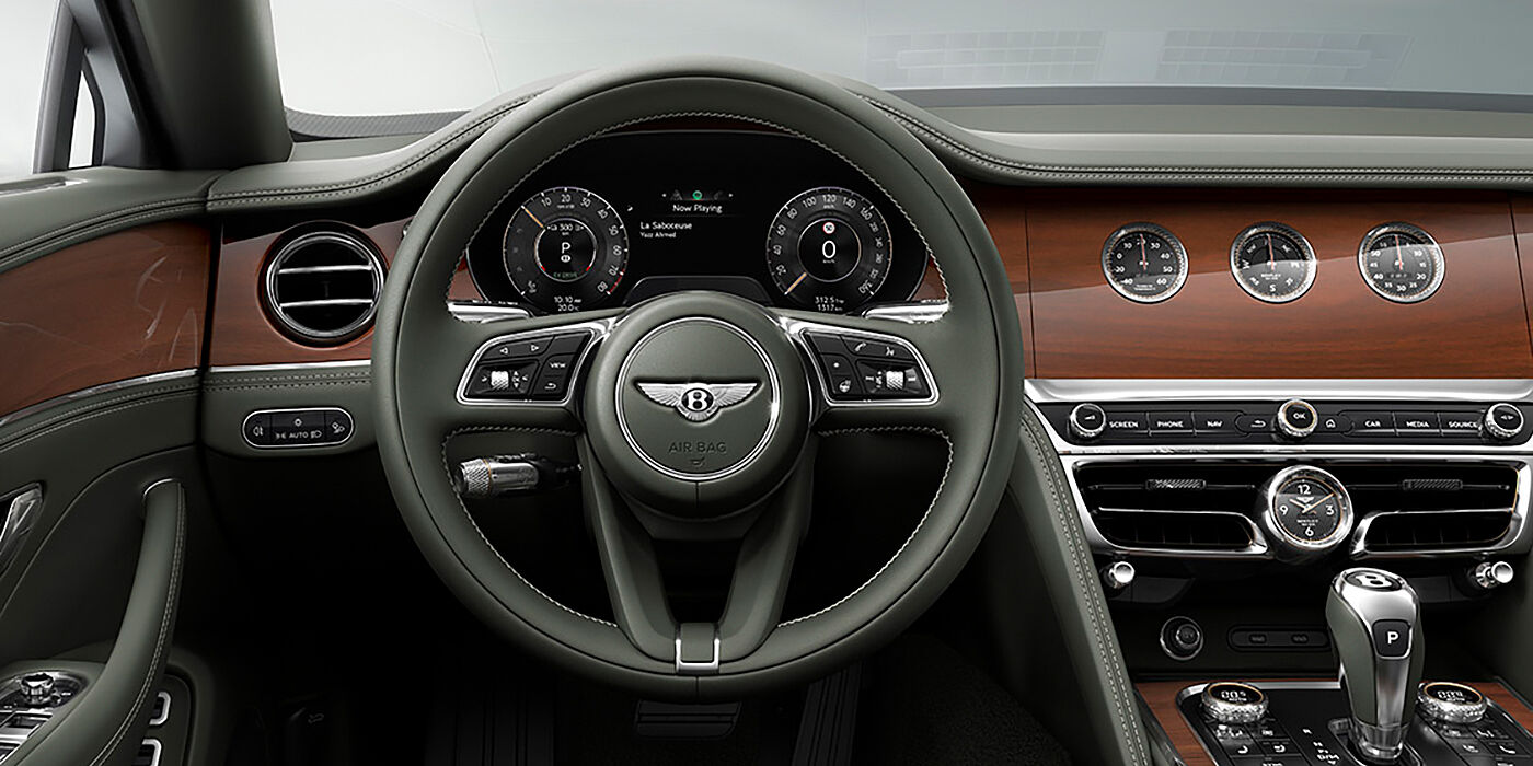 Gohm Sportwagen GmbH | Bentley Singen New Bentley Flying Spur sedan front cabin in Cumbrian Green hide and Crown Cut walnut veneer showing steering wheel and Rotating Display with three clocks on face