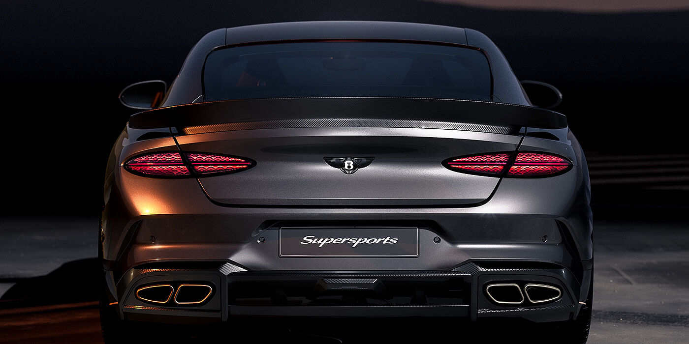 Gohm Sportwagen GmbH | Bentley Singen Bentley Supersports rear view with illuminated rear lamps, spoiler and black Bentley badge in Anthracite paint against a dark grey and red background