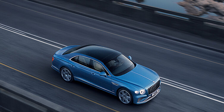 Gohm Sportwagen GmbH | Bentley Singen New Bentley Flying Spur Azure sedan in Light windsor blue paint by Mulliner, with 22 inch Azure wheels seen from overhead driving dynamically on a country road