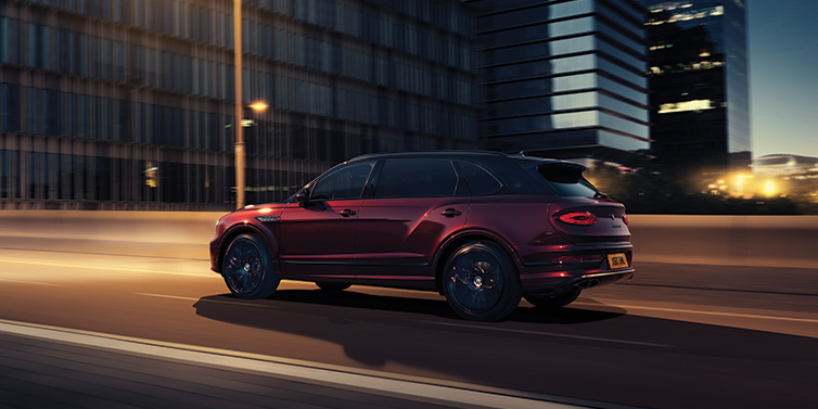 Gohm Sportwagen GmbH | Bentley Singen Bentley Bentayga Extended Wheelbase Mulliner SUV in Cricket Ball red paint driving dynamically in city at night