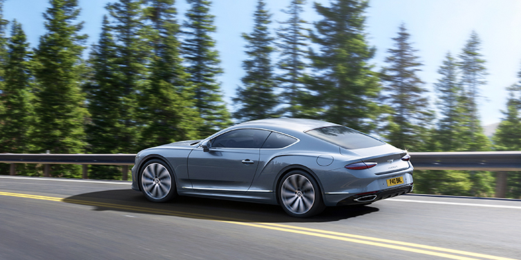 Gohm Sportwagen GmbH | Bentley Singen New Bentley Continental GT coupe in Silverlake paint, seen from the rear, driving dynamically on a tree-lined road